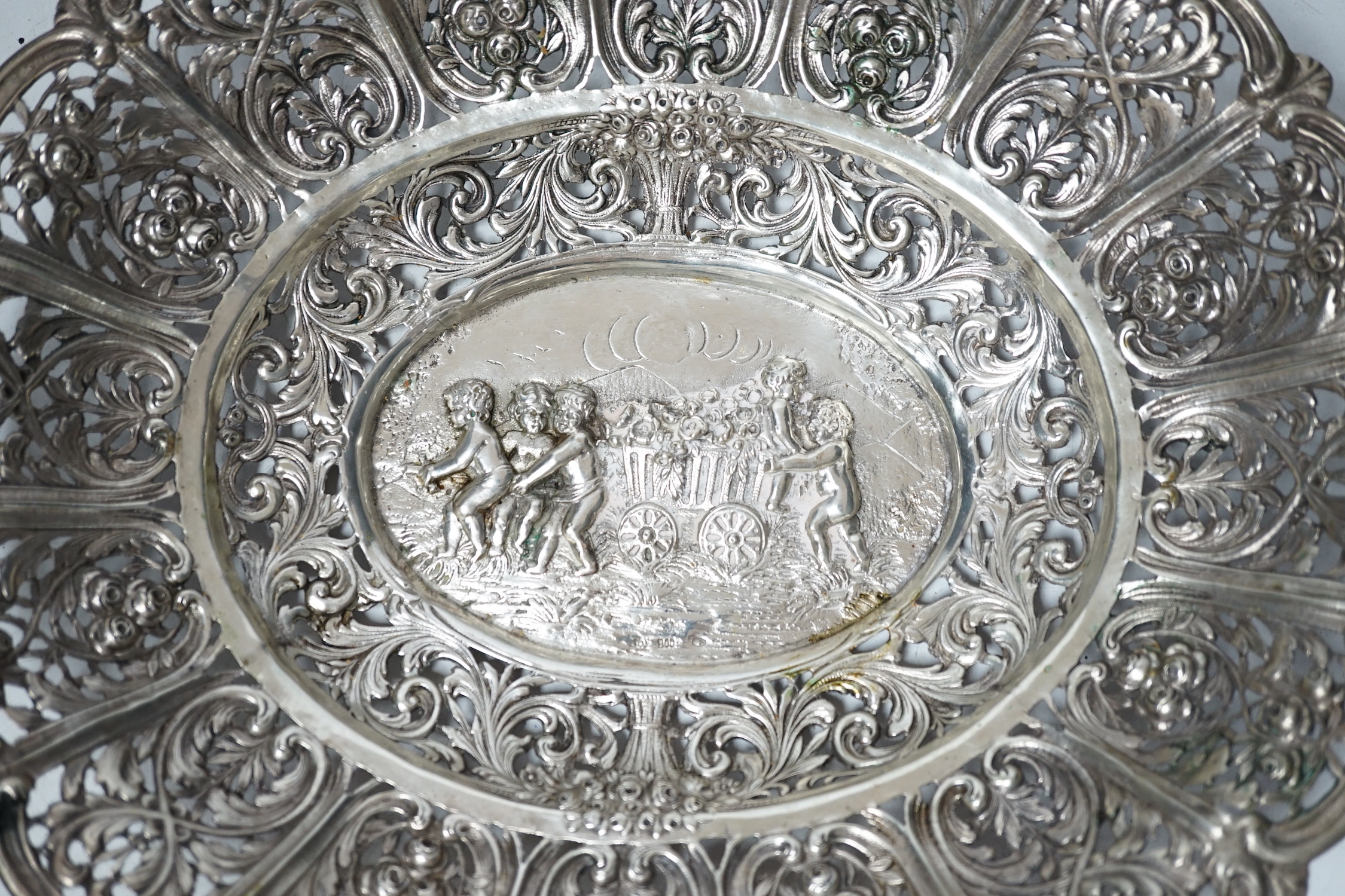 An early 20th century German 800 standard pierced white metal oval dish, decorated with putti and cart of flowers, 29.7cm, 13.2oz.